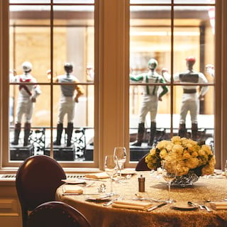 Una mesa de cena formal junto a una gran ventana rodeada de figuritas de jinetes