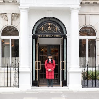 Smiling doorman in a red-coat under a black arched ironwork door