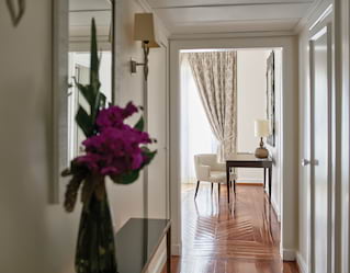 In the foreground a vase of bougainvillea blushes dark pink. Polished floors lead along a corridor to a light filled room