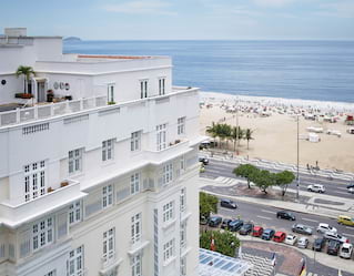 Calm blue sea laps the bustling Copacabana Beach. People stroll the sidewalk. Its pattern is repeated on the hotel's forecourt