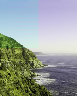 Ocean road curving around a sloping cliff beside a calm ocean at sunset