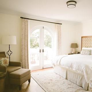 Sunlight pours through arched glazed double doors into a deluxe king bedroom at the El Encanto hotel