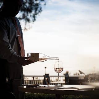Waiter pouring white wine into a glass with view of blue skies beyond