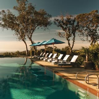 Outdoor infinity pool surrounded by sun beds and blue parasols