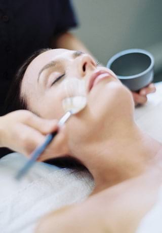 Close-up of a woman with closed eyes receiving a spa facial treatment>