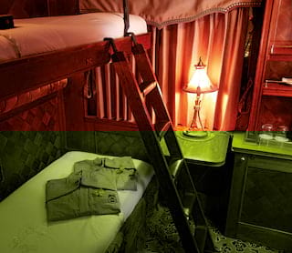 A night lamp glows in a Pullman Cabin, with crisp linen on the bunk beds and complimentary pyjamas, folded and ready.