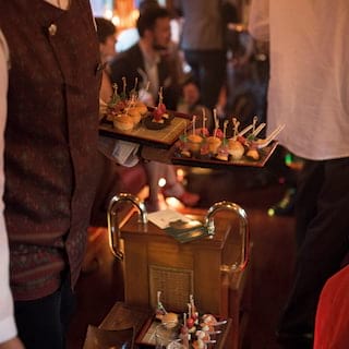 Close-up of a barman in a waistcoat serving canapés to guests in a train carriage