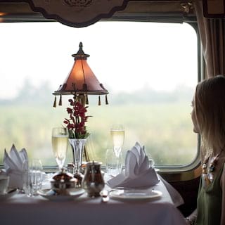 Lady at a table with two champagne glasses gazing out a train window