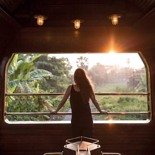 Lady looking out of an open-air train observation carriage at the sunrise beyond