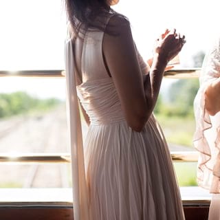 Lady in a light pink dress standing against brass railings in an open-air carriage