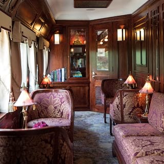 Wood-panelled lamplit saloon with ornate silk furnishings and bookshelves