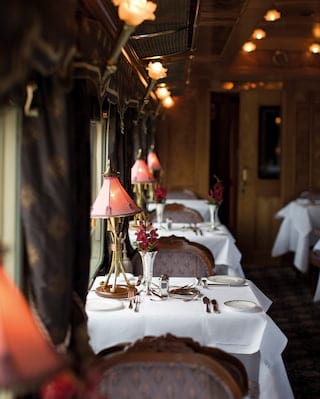 Rows of formal dining tables lining a luxurious train restaurant carriage