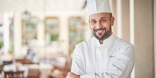 Michelin-starred executive chef, the native Sicilian Roberto Toro, smiles at the camera in his chef's whites and toque hat