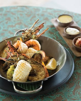 Close-up of a lobster dish in a jade coloured bowl next to a selection of dips