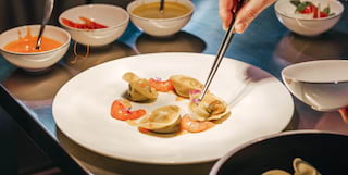 A fine dish of seafood pasta is assembled on a simple white plate on a shiny steel kitchen worktop