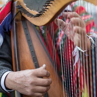 Close-up of two hands playing a wooden carved harp