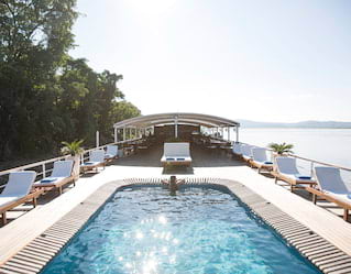 Glittering surface of an oval-shaped pool lined by sunbeds on a ship's top deck