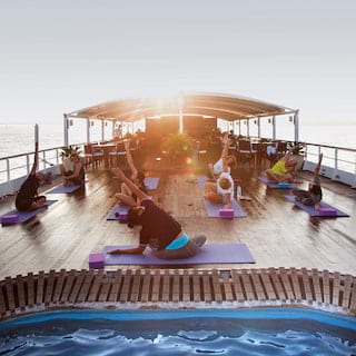 Ladies in yoga poses on purple yoga mats on the top deck of a ship at sunrise