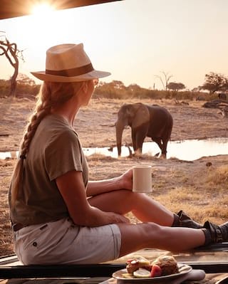 A guest enjoys her breakfast watching an elephant at the water hole nearby