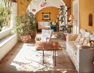 Dappled light filters through a cane and bougainvillea loggia roof. Pink petals dusting the floor like confetti among the sofas